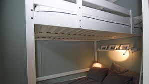 A bunk bed with a lower bunk and a single bed. There is a wall-mounted shelf with pictures and a reading light. - Stay.plus King Street (Kristiansand)