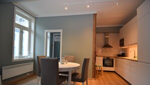 A modern kitchen with white cabinets, a built-in oven, and a dining area with a round table and chairs. - Stay.plus King Street (Kristiansand)