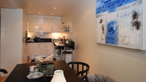 Una cocina moderna con armarios blancos, una mesa de comedor con sillas y un cuadro abstracto grande en la pared.