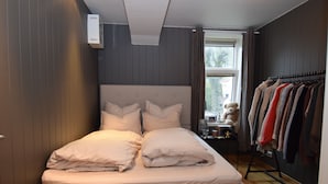 Un dormitorio con cama, ventana, mesita de noche y perchero.