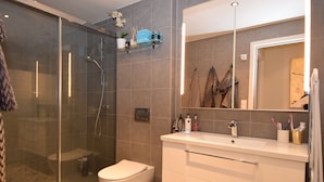 Un baño moderno con ducha envuelta en vidrio, inodoro blanco y tocador con espejo.