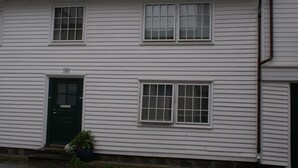 Une maison blanche à deux étages, avec une porte verte et deux fenêtres à l’étage supérieur.