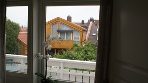 Une fenêtre donnant sur une maison jaune, un balcon avec une balustrade blanche et un pot d’orchidée.