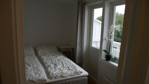 Une petite chambre avec un lit simple, une fenêtre, une table de chevet et une plante en pot.