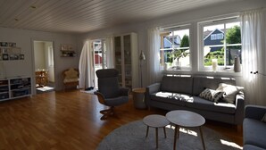 Een ruime woonkamer met een grijze bank, een ronde salontafel en een groot raam met gordijnen.