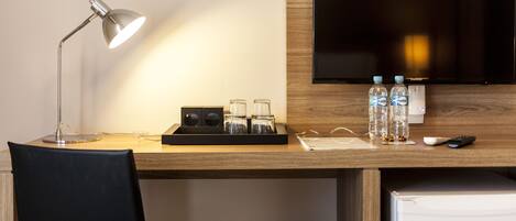 A hotel room with a desk, a lamp, a TV, and a mini-fridge.