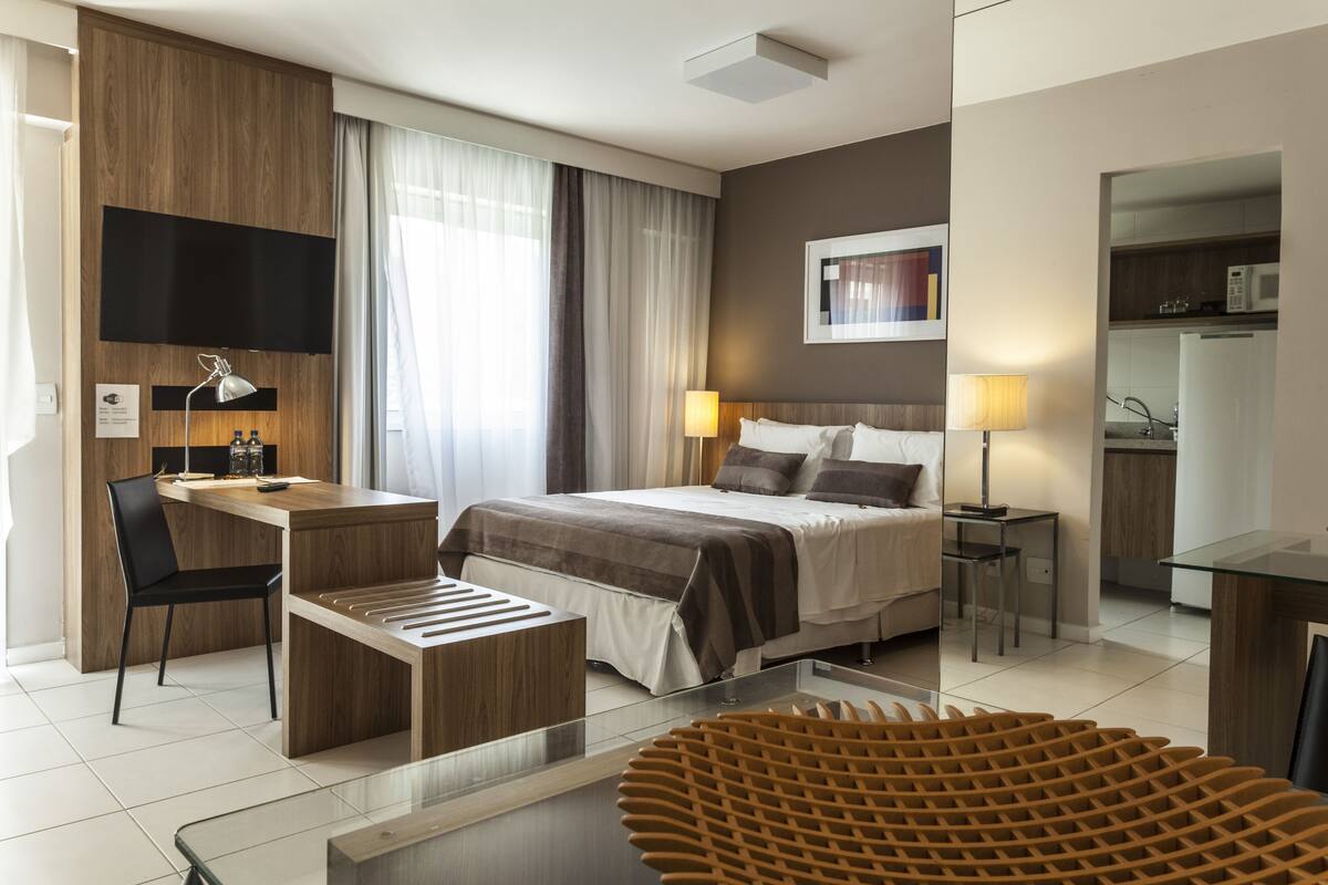 A modern hotel room with a bed, desk, chair, and a glass dining table.