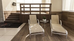 Un hall d’hôtel comprenant un comptoir d’accueil, deux fauteuils, une petite table avec une plante et un escalier menant à un étage supérieur.