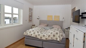Un dormitorio con cama, televisor, cómoda y ventana con vista a edificios.