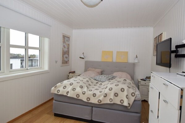 Un dormitorio con cama, televisor, cómoda y ventana con vista a edificios.