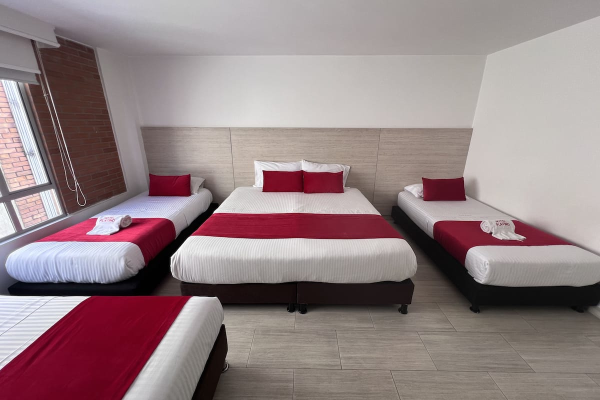 Ein Hotelzimmer mit drei Betten, jeweils mit weißer und roter Bettwäsche, und einem großen Fenster, das für natürliches Licht sorgt.