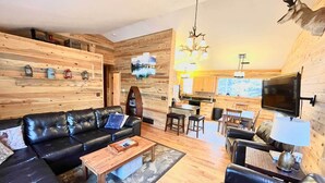 A modern living room with a black leather sofa, a wooden coffee table, and a TV mounted on the wall. - 'Bobcat Trail Cabin' on 3 Acres in Como! (Como)