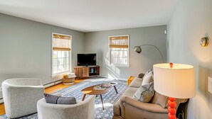 Ein Wohnzimmer mit Sofa, Sesseln, Couchtisch, Fernseher und Lampe.