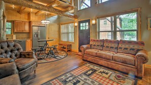 A rustic cabin interior with a wooden dining table, leather sofa, and a large window. - Timber Home: Walk to Slopes & N Conway Shops! (North Conway)
