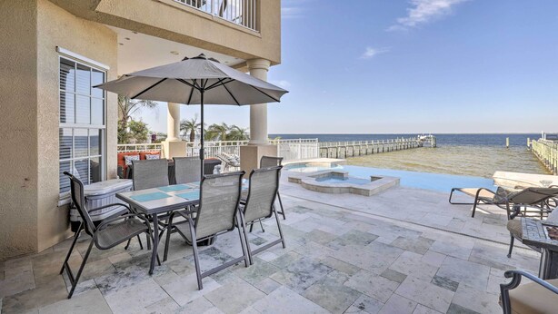 Um pátio com móveis, piscina e vista para o oceano.