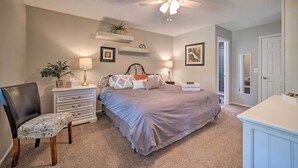 Ein Schlafzimmer mit Bett, Stuhl, Kommode, Deckenventilator und einer Tür.