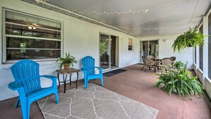 Ein überdachter Patio-Bereich mit blauen Adirondack-Stühlen, einem Tisch und Blumentöpfen.