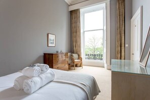 A hotel room with a bed, a wooden dresser, a chair, and a large window with curtains. - Airy & Stylish New Town Apartment (Edinburgh)