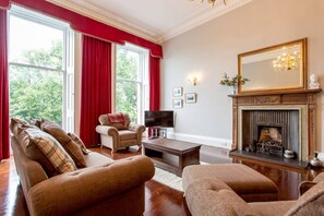 A living room with a fireplace, a television, and a large window with red curtains. - Airy & Stylish New Town Apartment (Edinburgh)