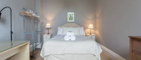 Un dormitorio ordenado con cama, lámparas de noche, escritorio y un tendedero de pared.