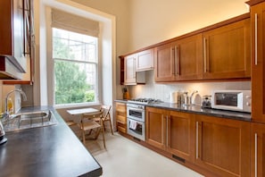 A modern kitchen with wooden cabinets, a gas stove, a microwave, and a window providing a view of greenery outside.