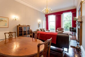 A dining room with a wooden table and chairs, a red upholstered sofa, and a fireplace with a mantle.