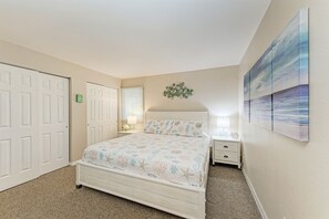 A bedroom with a bed, two nightstands, a wall-mounted artwork, and a door.