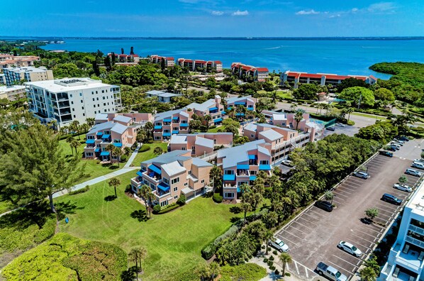 An aerial view of a resort with multiple buildings, a parking lot, and a view of the ocean.