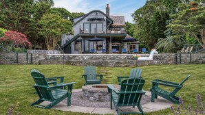 Una casa con un patio que incluye sillas tipo Adirondack, un brasero y un muro de piedra.