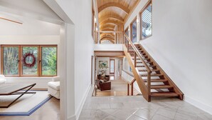Un interior espacioso con un alto techo, una escalera de madera y grandes ventanales que ofrecen vistas al exterior.
