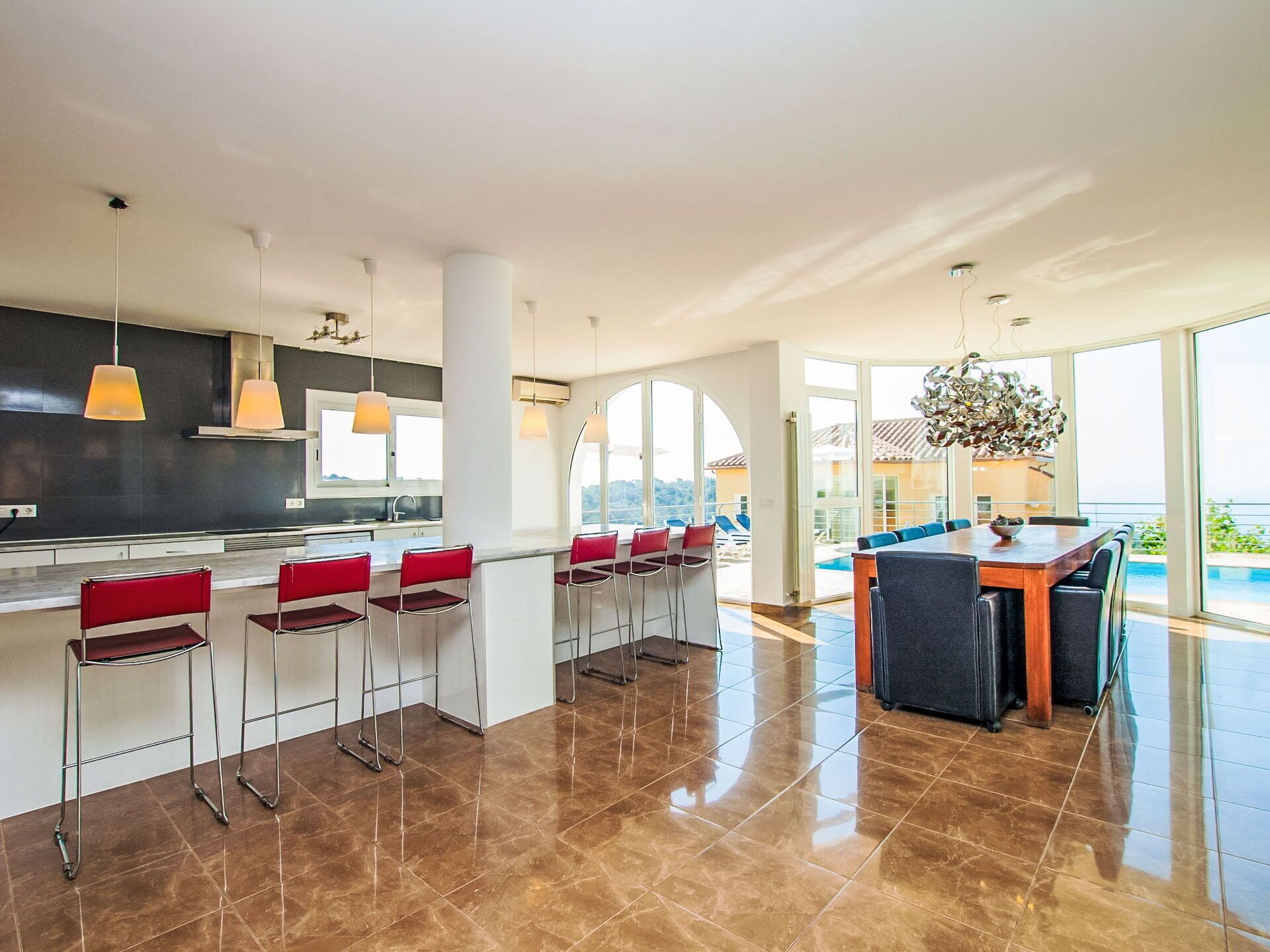 A modern kitchen with a bar area, large windows, and a view of the sea.