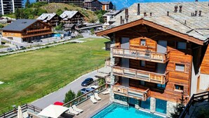 Una cabaña de madera con piscina, rodeada por una terraza con sillones y sombrillas.