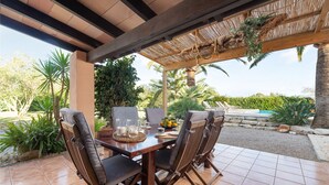 Um pátio externo com mesa de madeira, quatro cadeiras e um pergolado.