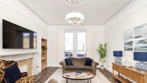 Una sala de estar con sofá, sillón, mesa de centro, televisor, chimenea y vista a la calle.