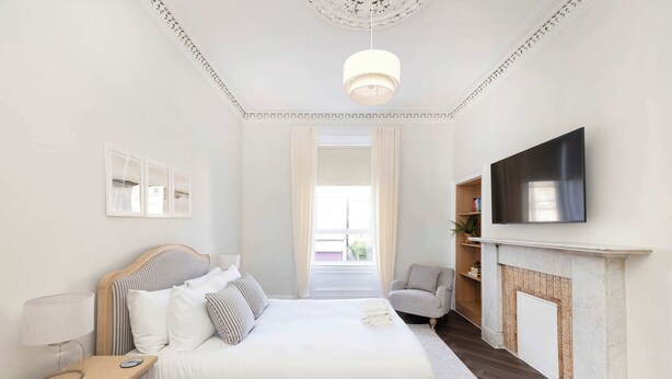 Un dormitorio con cama, mesita de noche, lámpara, televisión, chimenea y vistas al exterior.