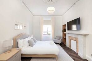 Une chambre à coucher comprenant un lit, une table de chevet, une lampe, une télévision, une cheminée et une vue sur l’extérieur.