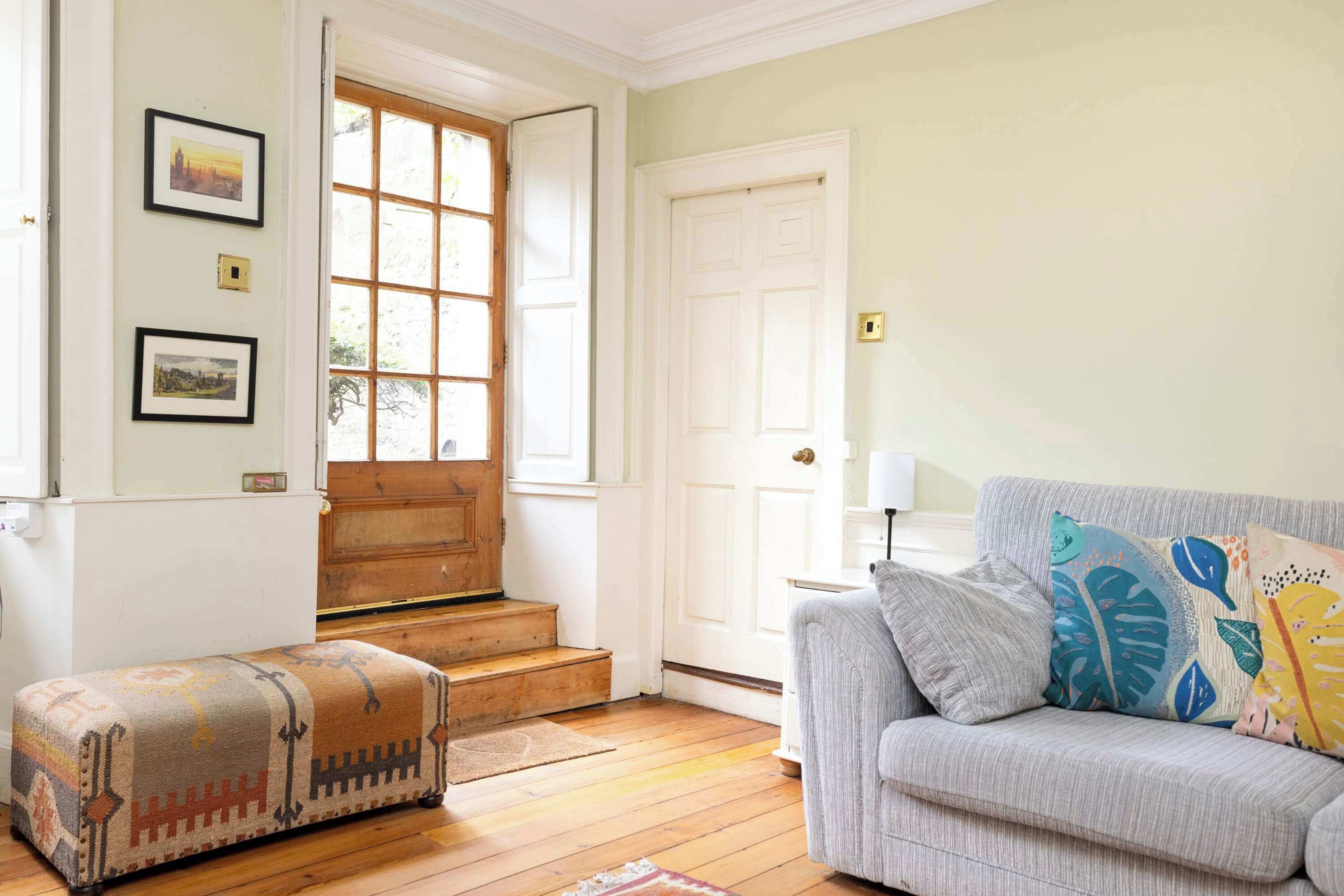 A living room with a sofa, ottoman, and a wooden staircase leading to a door.
