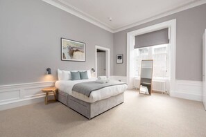 Un dormitorio con cama, mesita de noche, espejo y ventana.