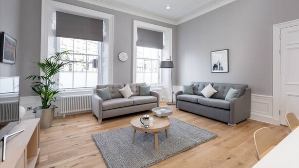 Ein modernes Wohnzimmer mit zwei grauen Sofas, einem Couchtisch, einer Topfpflanze und großen Fenstern.