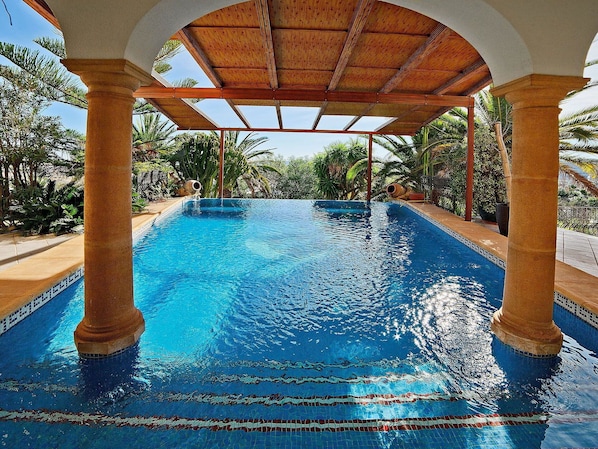 Relax by the serene pool surrounded by lush greenery and a shaded pergola.