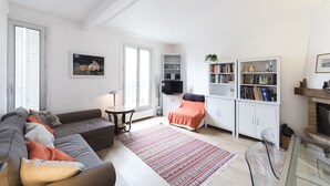 A living room with a sofa, a coffee table, and a fireplace. There are bookshelves and a television.