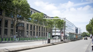 A street with modern buildings, a tram line, and a clear sky.