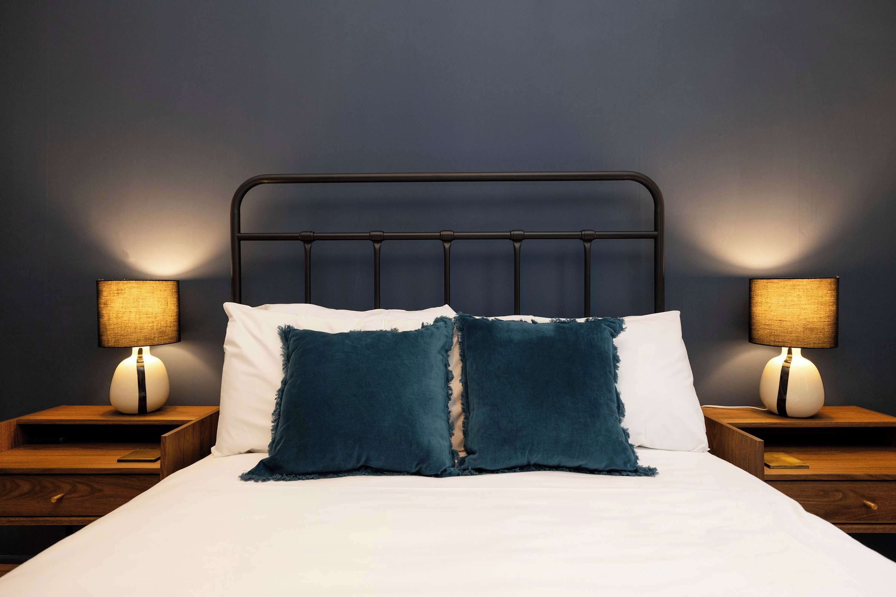 A neatly made bed with two pillows, a headboard, and two bedside tables with lamps.