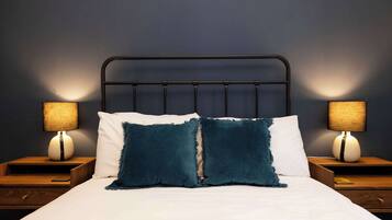 A neatly made bed with two pillows, a headboard, and two bedside tables with lamps.