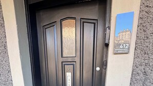 Una puerta negra con felpudo, buzón y placa con el número de la casa.
