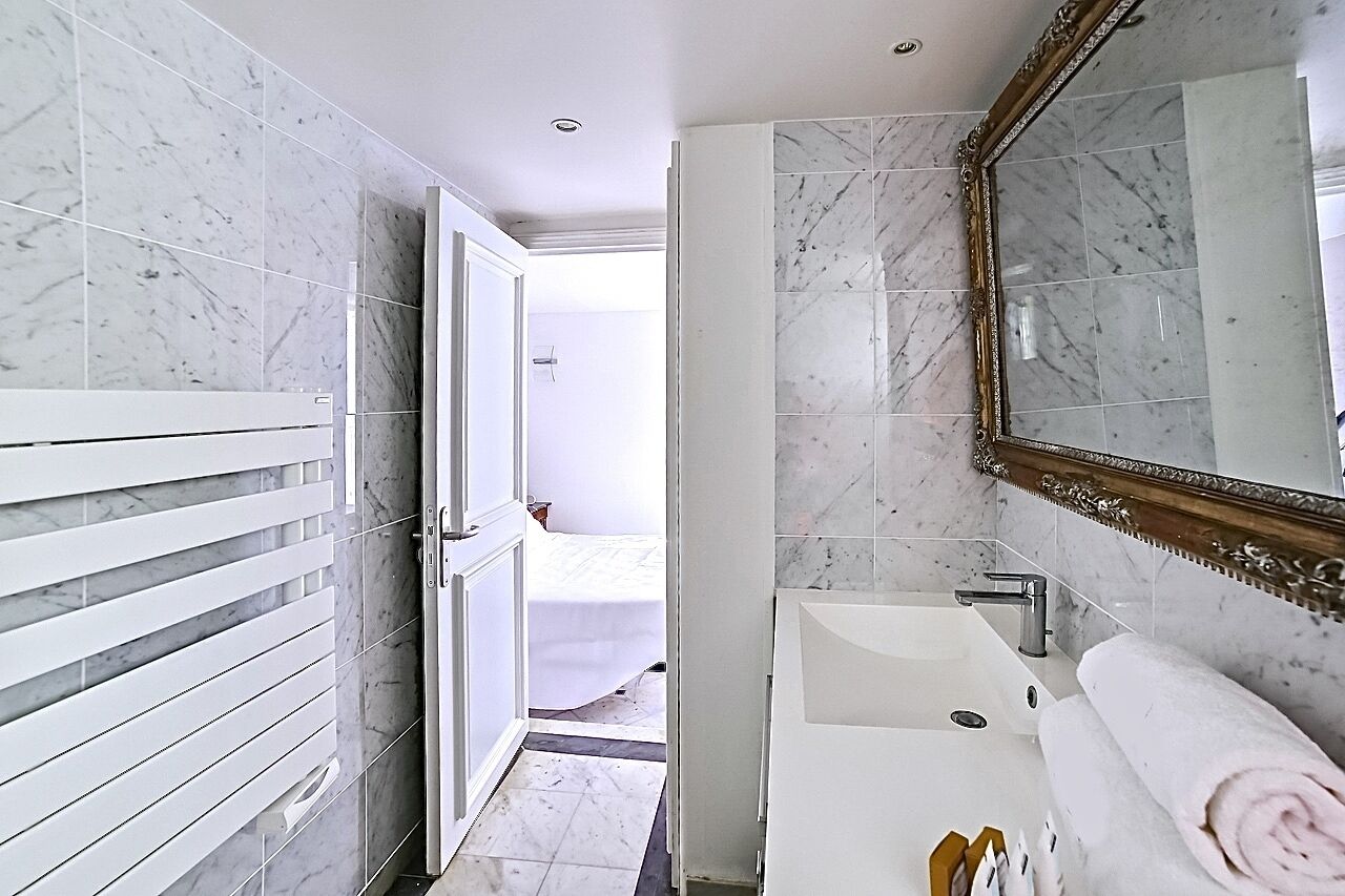 Une salle de bain avec un sol en marbre, un lavabo blanc, un grand miroir et une serviette posée sur le lavabo.