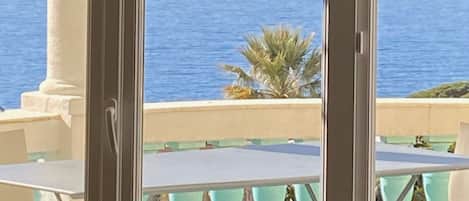 A balcony with a table and chairs, overlooking a body of water and distant mountains.