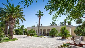 A courtyard with a stone pathway leading to a building with arches and a palm tree in the center. - Stunning private villa with hot tub, A/C, private pool, WIFI, TV, patio and pets allowed (Nardò)