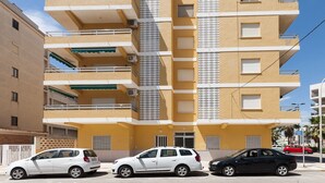 A multi-story residential building with balconies, a central air conditioning unit, and a street view with parked cars. - RIVER  - Apartment with sea views Free WiFi (Daimús)