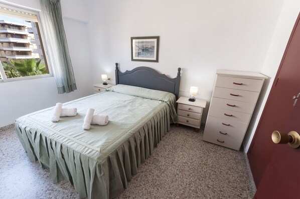 A bedroom with a bed, bedside tables, a dresser, and a window with a view of buildings. - RIVER - Apartment with sea views Free WiFi (Daimús)